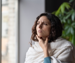 Upset sick woman standing at home touching swollen neck glands, having sore throat from virus